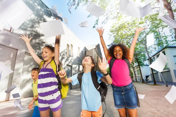 Diverse group of school kids throwing piles of paper happy exiting building
