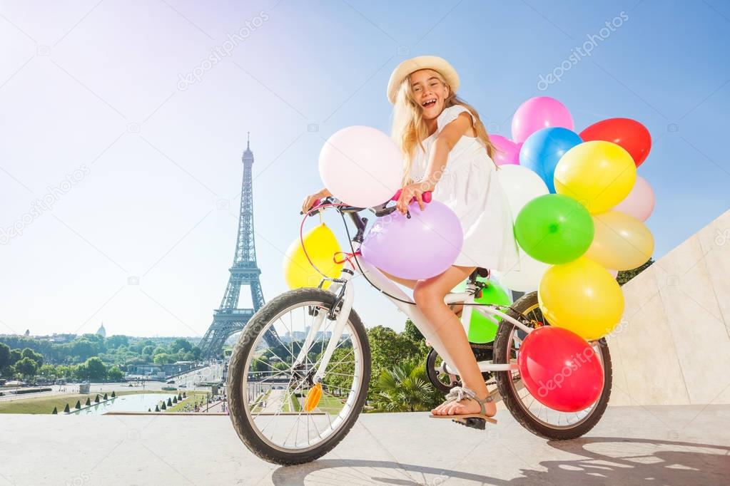 French girl cycling with colorful balloons bouquet against the Eiffel Tower in summertime