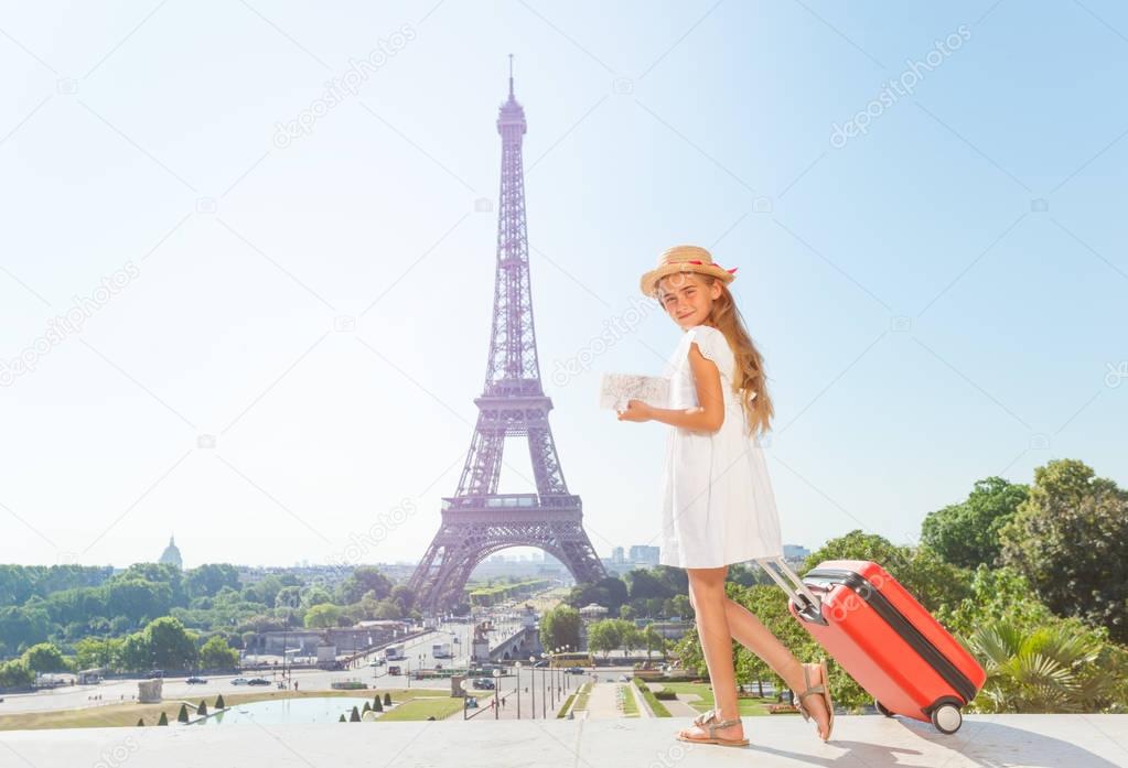 Preteen blond girl walking around Paris with suitcase and guide during summer vacation