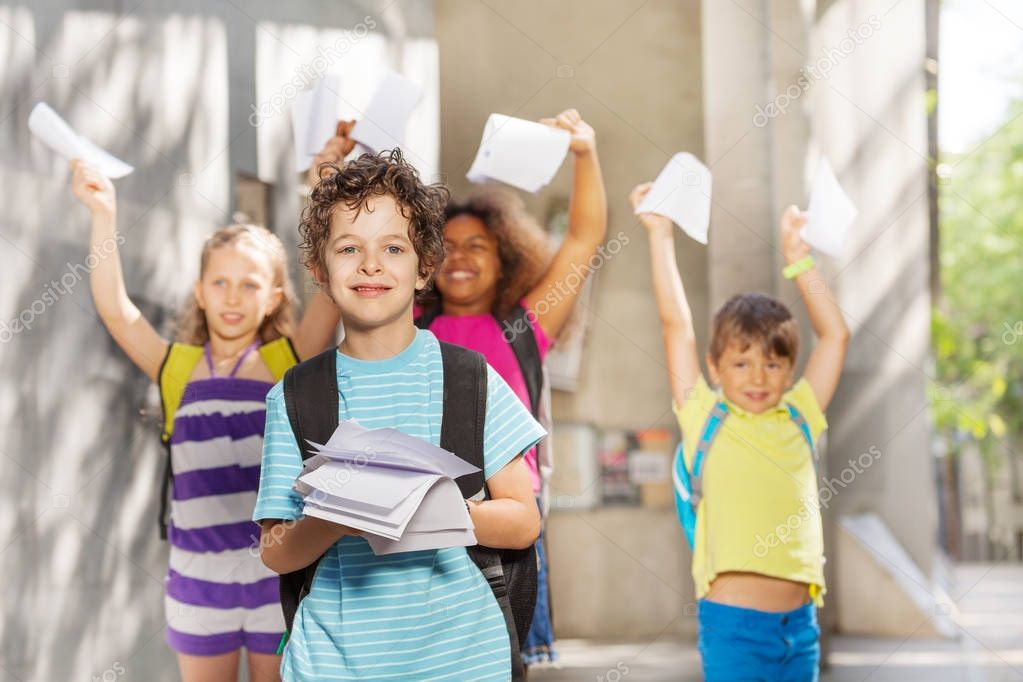 Nice handsome boy with paper near the school and group of friends on background