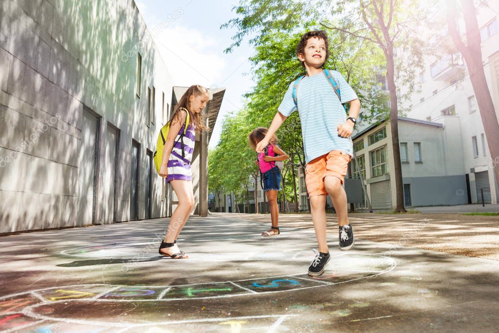 Children jumping on the hopscotch squares and numbers looking at camera with handsome boy on foreground