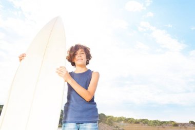 Sörf tahtası ile yakışıklı çocuk ayağa plaj portre üzerinde gökyüzü