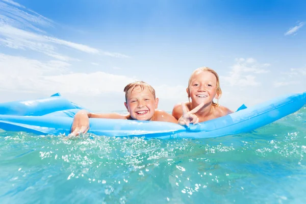 Two best friends laughing, swimming on blue matrass and splashing in clear sea water