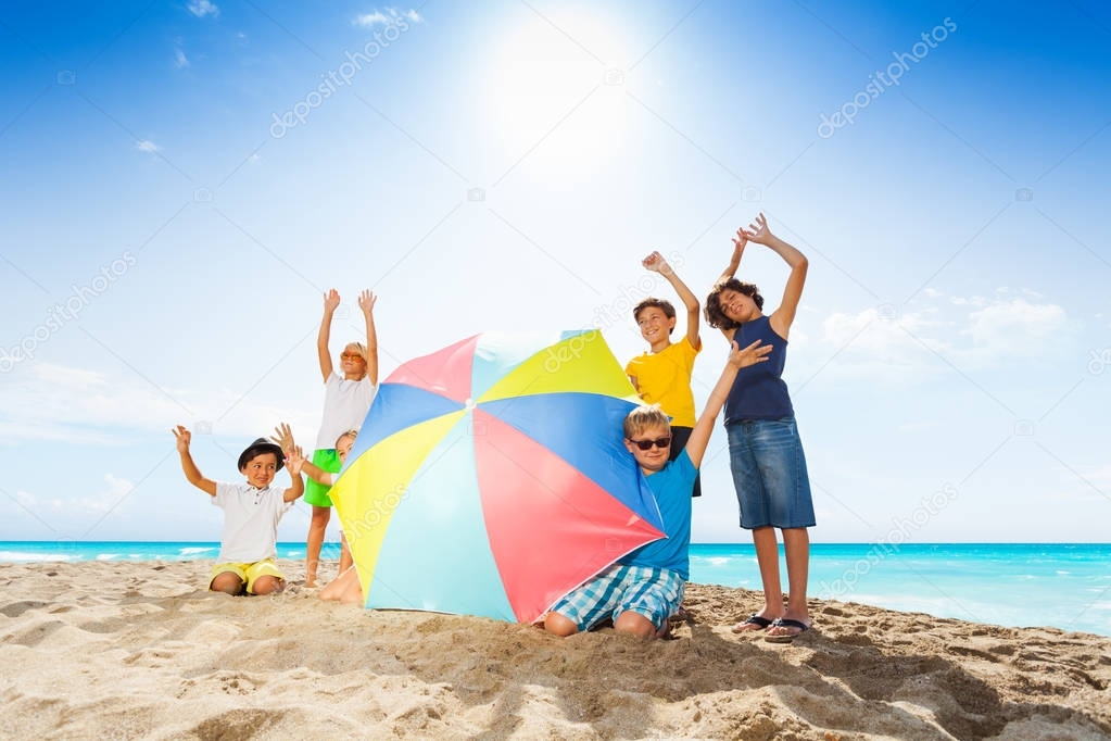 Group of kids standing with sun umbrella on beach and waving hands