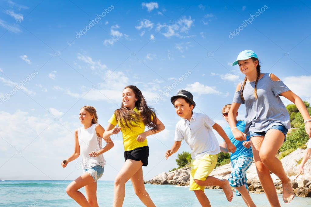 Group of happy kids running fast on the beach of the sea in sunny weather