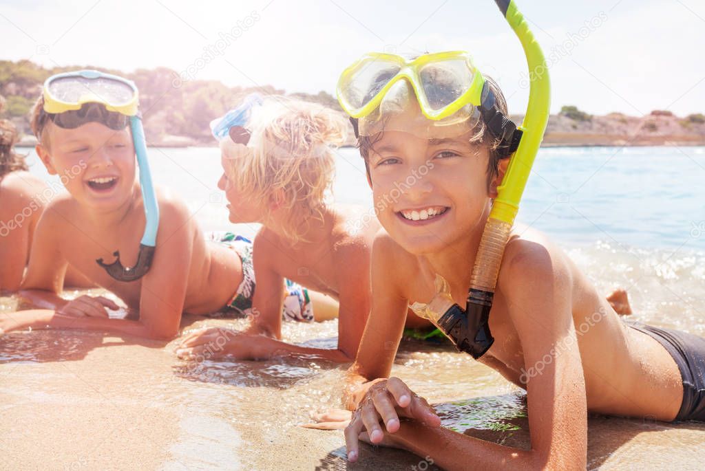 Boy with friends in scuba mask smiling laying on the sand and sea waves surge kids