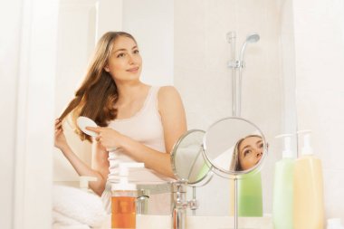 Genç ve güzel kadın banyoda ayna önünde uzun saçları fırçalama portresi