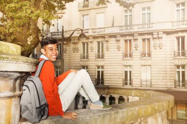 Paris sokakta oturan sırt çantası ile mutlu Afrika öğrenci