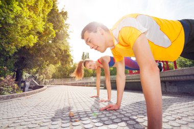Sportif genç çift, erkek ve kadın spor giyim, güneşli gün parkta tahta egzersiz yaparak portresi