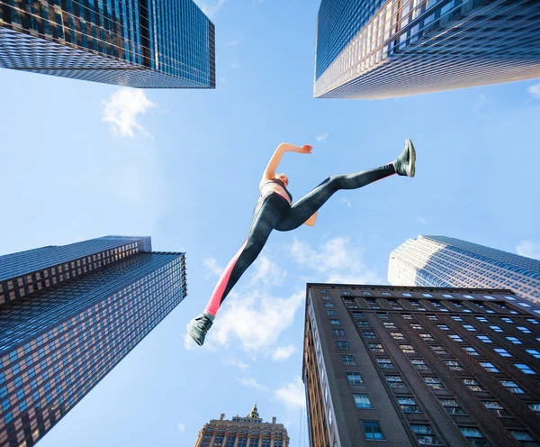 女性アスリートの低角度の都市景観に対してジャンプしながら空気のまま — ストック写真