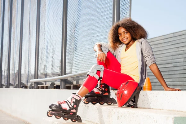 Rollerdrom でローラー スケートで階段の上に座って満足しているアフリカの女の子 — ストック写真