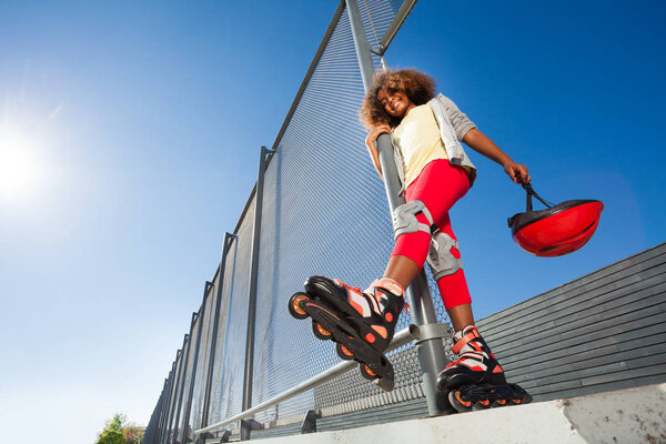 Low-angle view of preteen African girl in roller skates posing at skate park at sunny day
