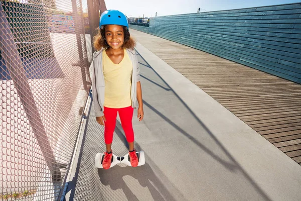 晴れた日に歩道にホバーボードを乗ってヘルメットで幸せなアフリカの女の子 — ストック写真