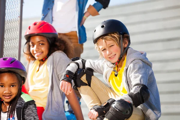 ローラー ヘルメットや防護服カメラ目線 友人と屋外スタジアムで座ってのプレティーンの少年 — ストック写真