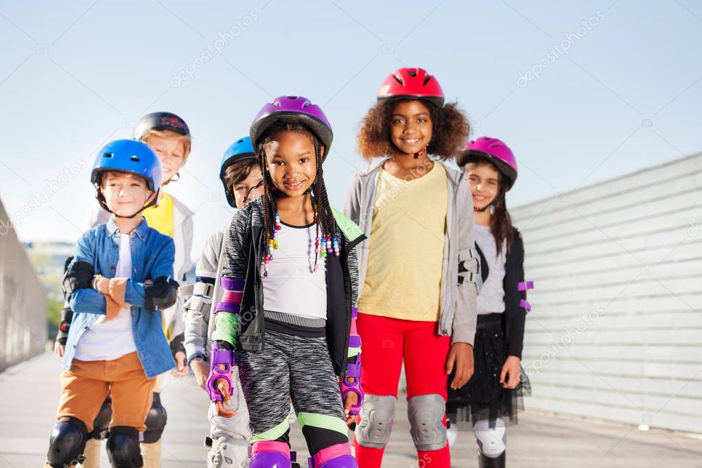 Group of happy sporty kids, preteen boys and girls in safety gear rollerblading outdoors