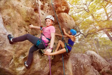 Young girls in helmets climbing a rock in forest area clipart