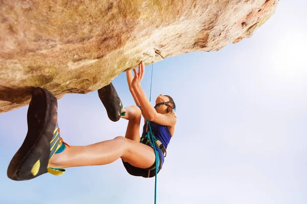 Low angle view of teenage girl rock climber training outdoors against blue sky