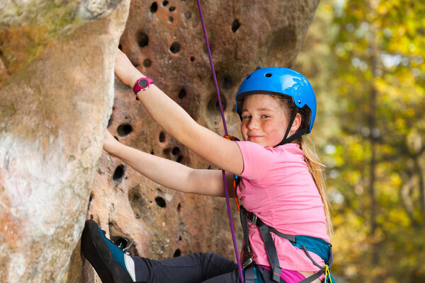 Close-up portrait of teenage girl in safety helmet climbing on the rock route in forest area