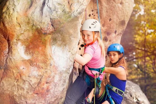 Female instructor of rock climbing with teenage girl training outdoors wearing helmets and harnesses