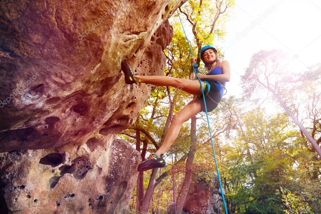 Bottom view of teenage girl in helmet rock climbing in forest area