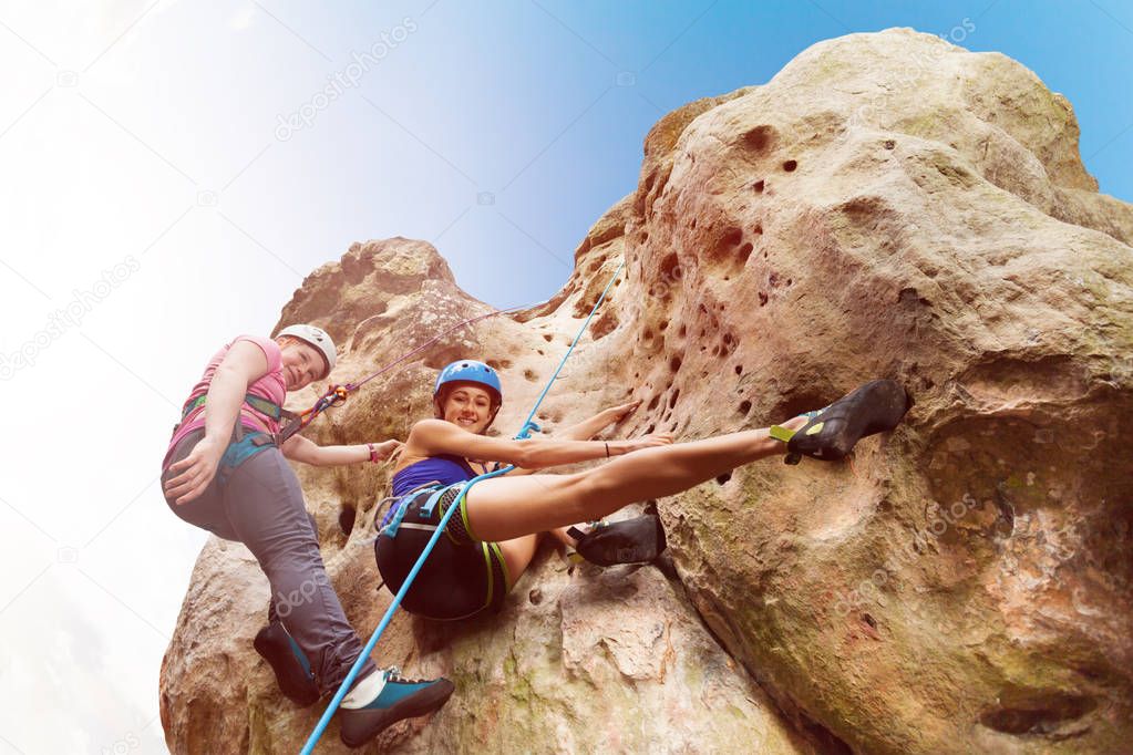 Bottom view portrait of female instructor teaching teenage girl climbing a rock with harnesses against blue sky