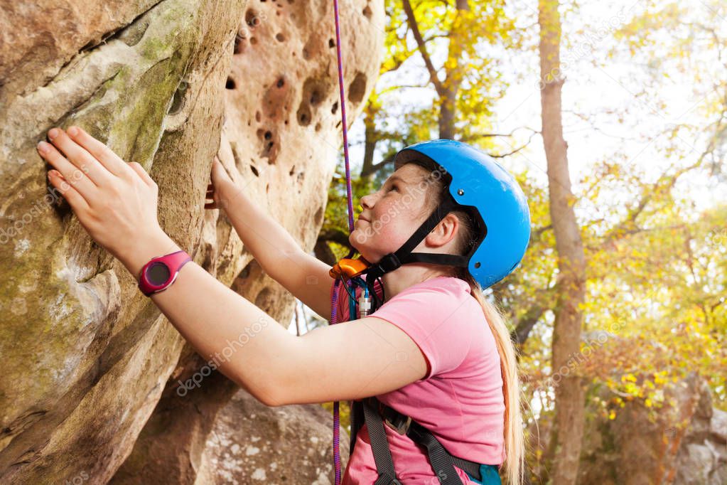 Teenage girl, rock climber in helmet, exercising outdoors at sunny day
