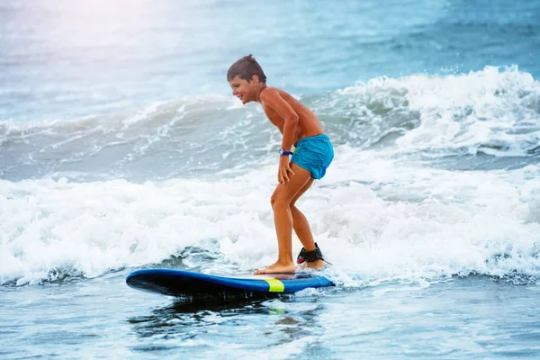 Мальчик стоит на доске для серфинга и учится ездить верхом. — стоковое фото