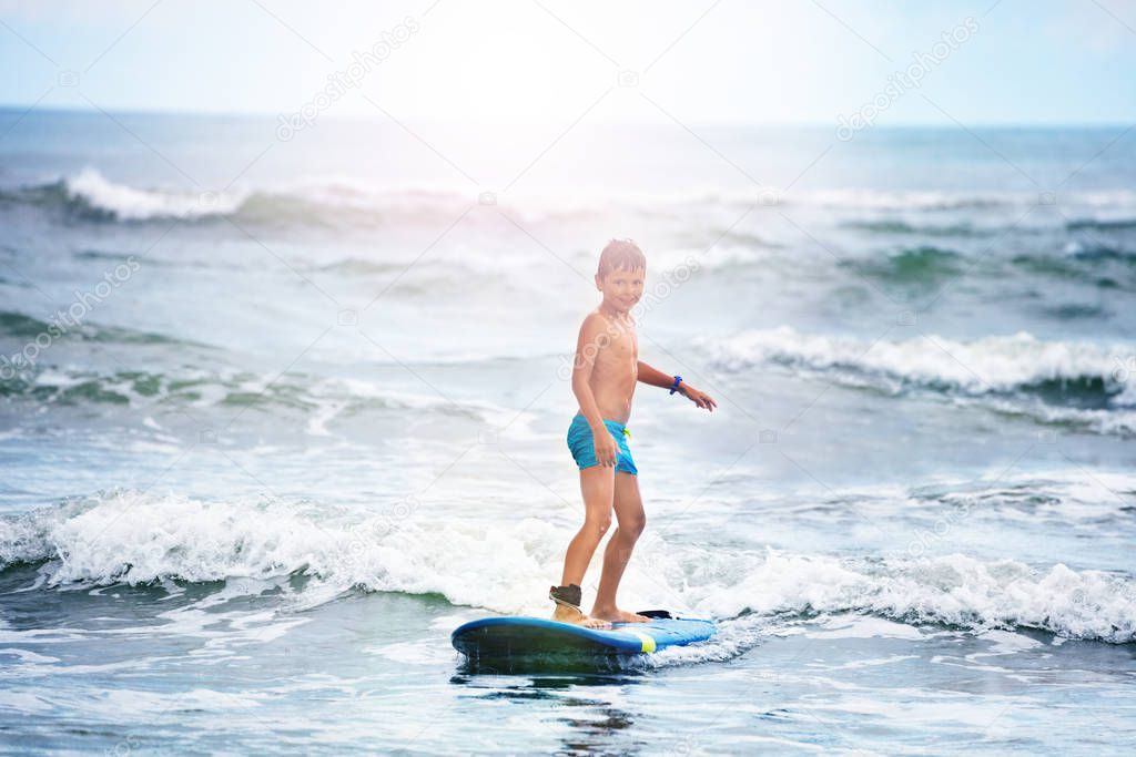 Little boy standing on surf board in the water