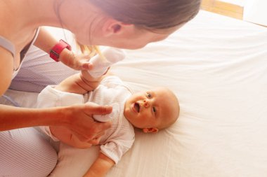 Young mother play with laughing infant on the bed