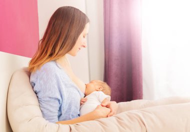 Mother feed newborn baby infant boy on the bed