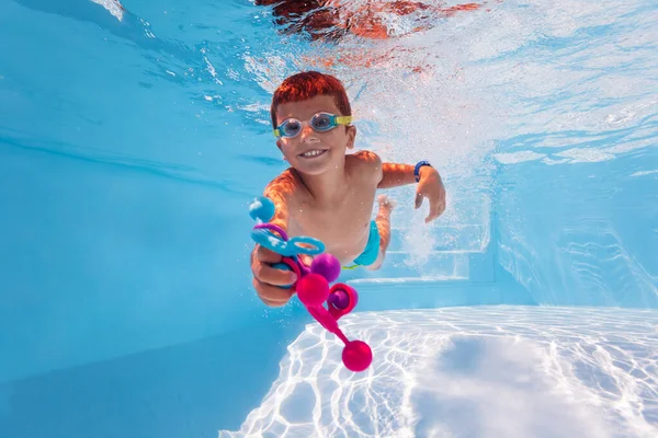 Child dive in a pool collecting toys wear googles — Stockfoto