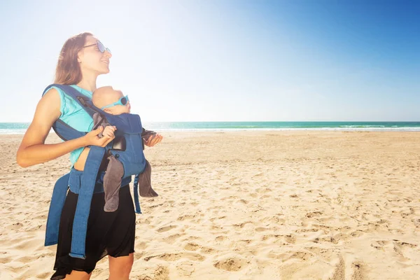 Mother and baby in carrier on the sunny sea beach — Zdjęcie stockowe