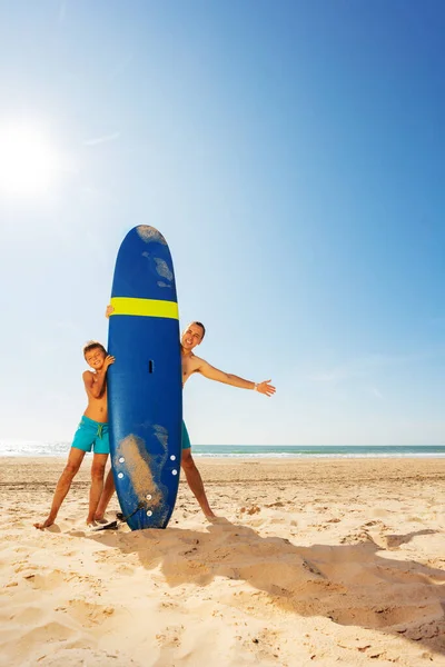 Padre e hijo detrás de tabla de surf en la playa de arena — Foto de Stock