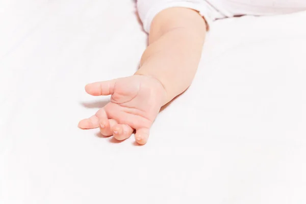 Piccola mano infantile posa sul letto lenzuolo bianco — Foto Stock