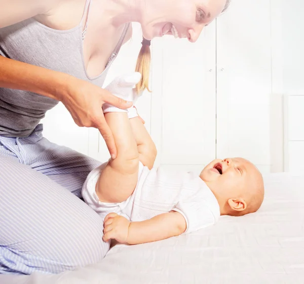 Young mother play with laughing baby on the bed — Stockfoto