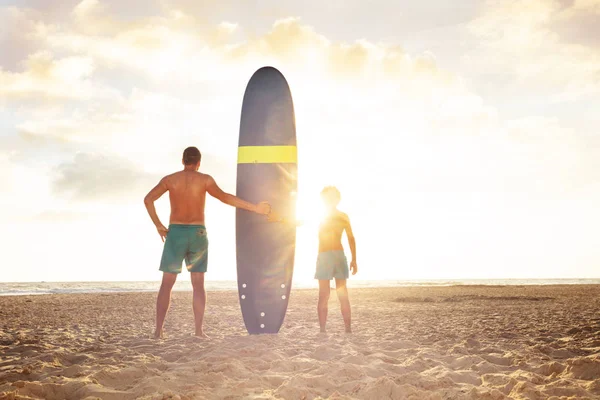 Sunset father and son stand with surf board on sea — Φωτογραφία Αρχείου