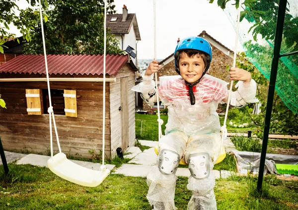 Overprotective boy in bubble wrap swing on swings — Stock Photo, Image