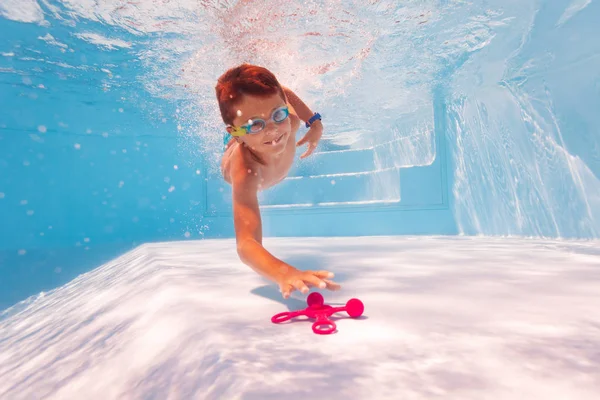 Милый мальчик ныряет и плавает в поисках игрушки на дне бассейна — стоковое фото