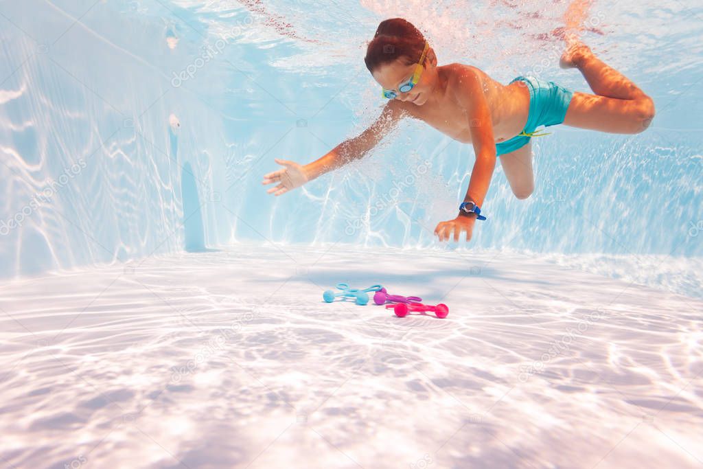 Boy dive underwater take toys in pool with googles