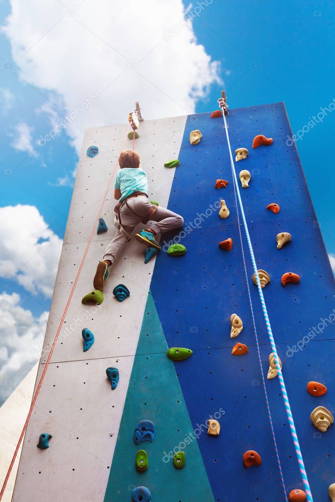 Little child boy climb on rock climbing high wall