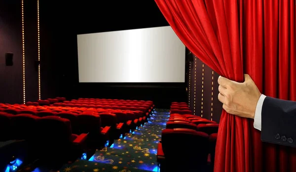 Cinema seats and blank screen with hand opening red curtain — Stock Photo, Image