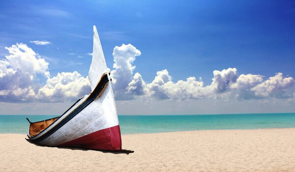 Небольшая деревянная лодка на пляже под облачным голубым небом
