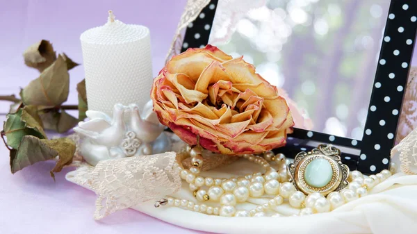 Torra rose på en bakgrund av speglar, fotoramar, vintage hänge pärlor, tyg är rosa, lila, champagne, vit. — Stockfoto