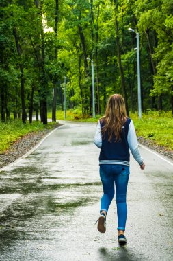 Bir kız sokakta çalışır. Bir yağmur sonra ıslak kaldırım. Kot rahat kıyafetler kız.