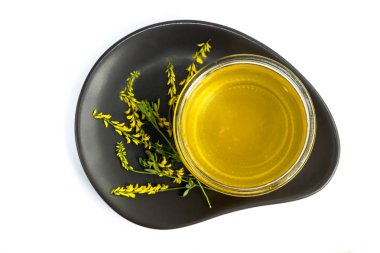 Cam Kavanoz renkler sarı yonca ile beyaz bir arka plan üzerinde siyah bir tabakta bal ile.