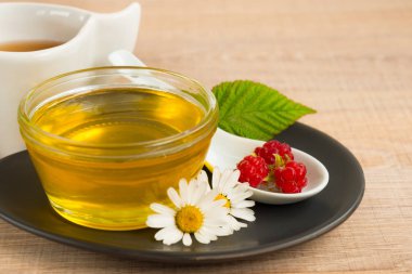 Bir fincan tabak tatlım. Kaşık bal, ahududu, papatya, derevyanny arka plan damla.