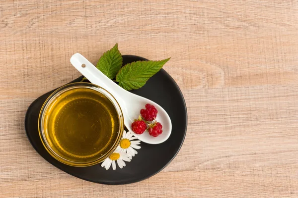 Bir fincan tabak tatlım. Kaşık bal, ahududu, papatya, derevyanny arka plan damla.