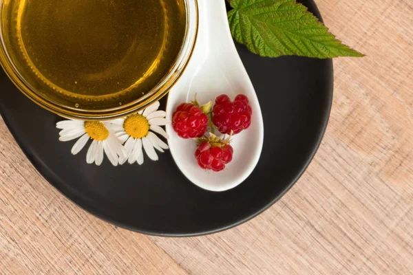 Bir fincan tabak tatlım. Kaşık bal, ahududu, papatya, derevyanny arka plan damla.