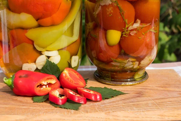 Banche con pomodori in scatola e peperoni nell'olio. Sullo sfondo del giardino . — Foto Stock