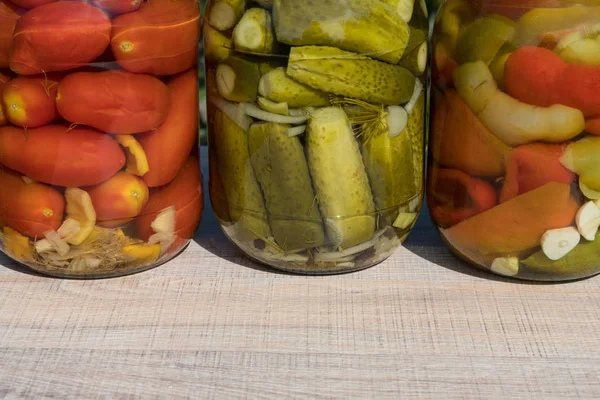 Банки консервовані овочі, помідори, огірки, перець болгарський. На дерев'яну столову на фоні саду — стокове фото